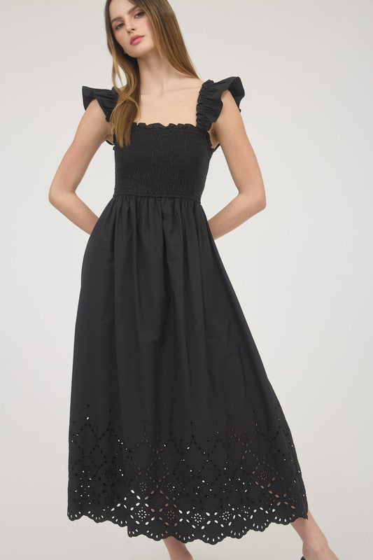 Model wearing black smocked midi dress with ruffle straps and eyelet hem – front view