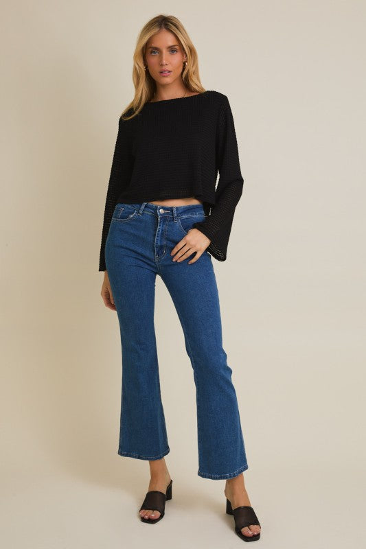 Woman wearing a black top and blue jeans against a beige background