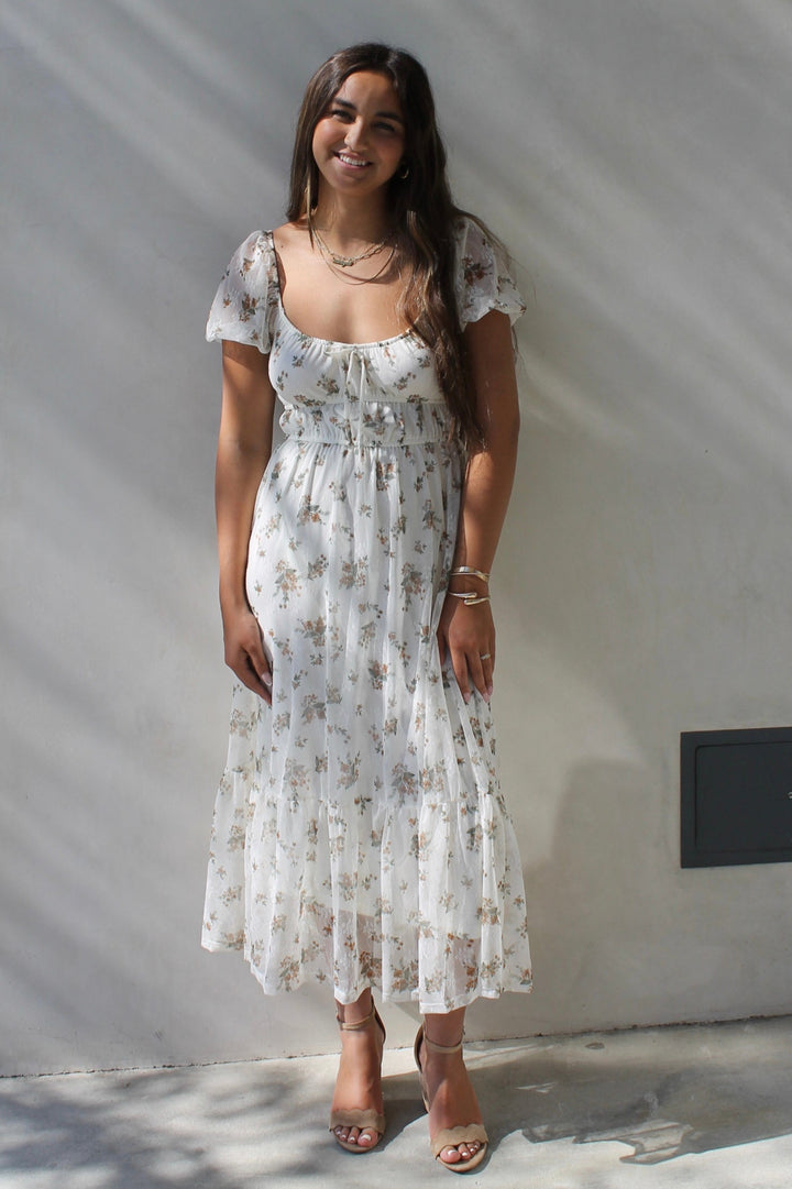 Woman in a floral dress standing against a white wall
