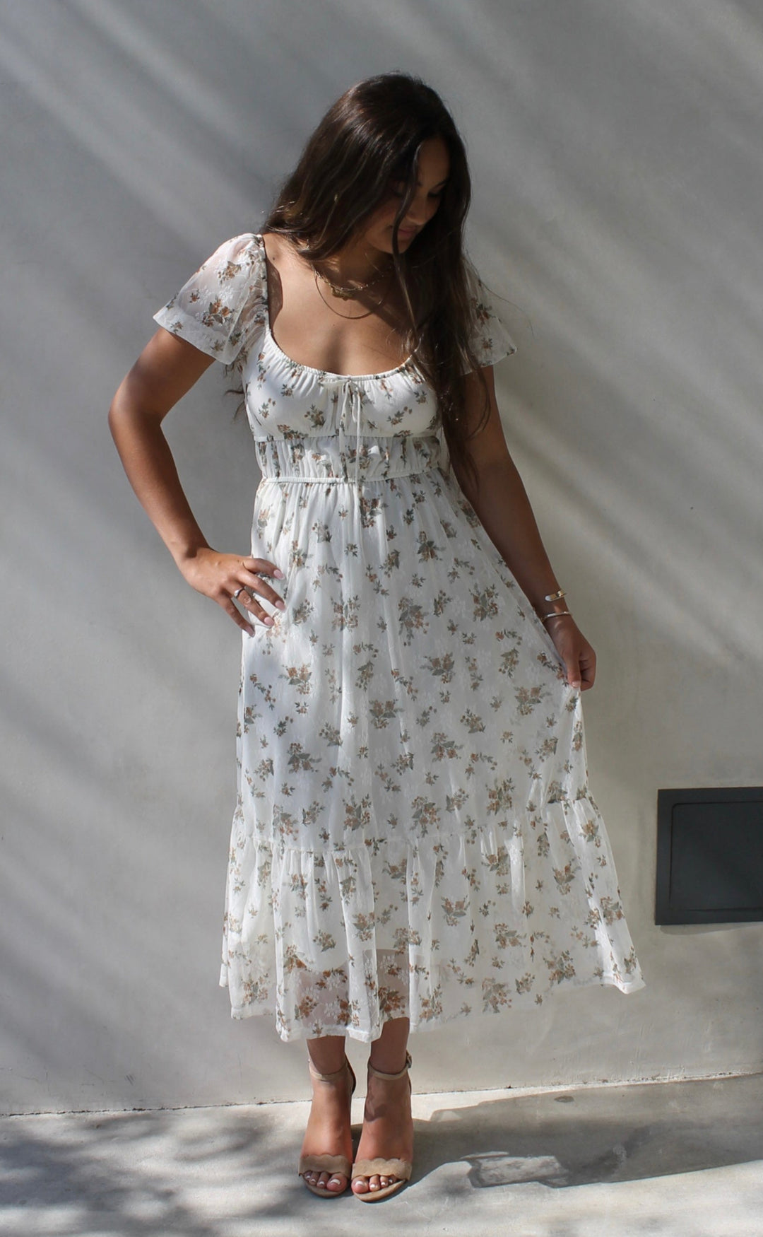 Woman in a white floral dress standing against a white wall.