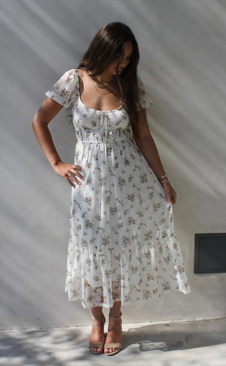 Woman in a white floral dress standing against a white wall.