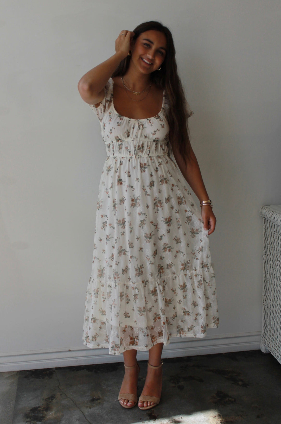 Woman in a floral dress standing indoors with a neutral background
