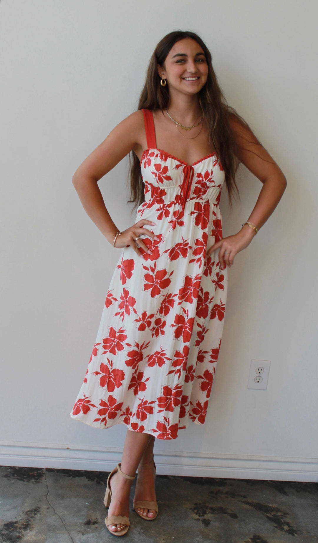 Woman wearing a red floral dress standing against a white wall.