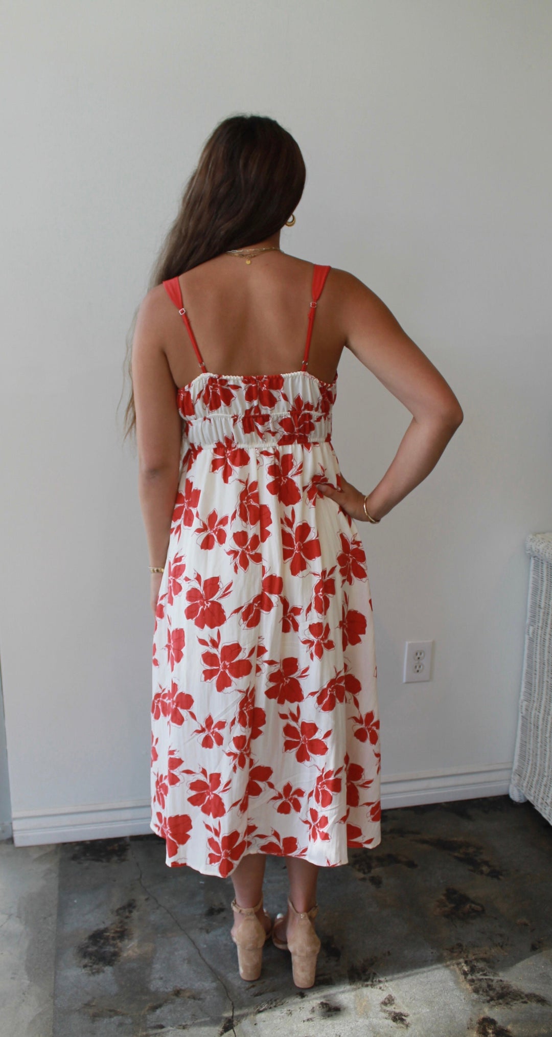 Woman wearing a white dress with red floral pattern in a room.