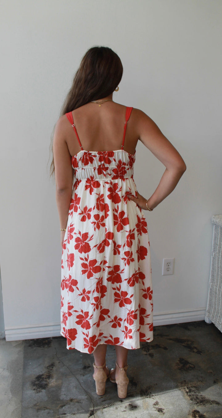 Woman wearing a white dress with red floral pattern in a room.