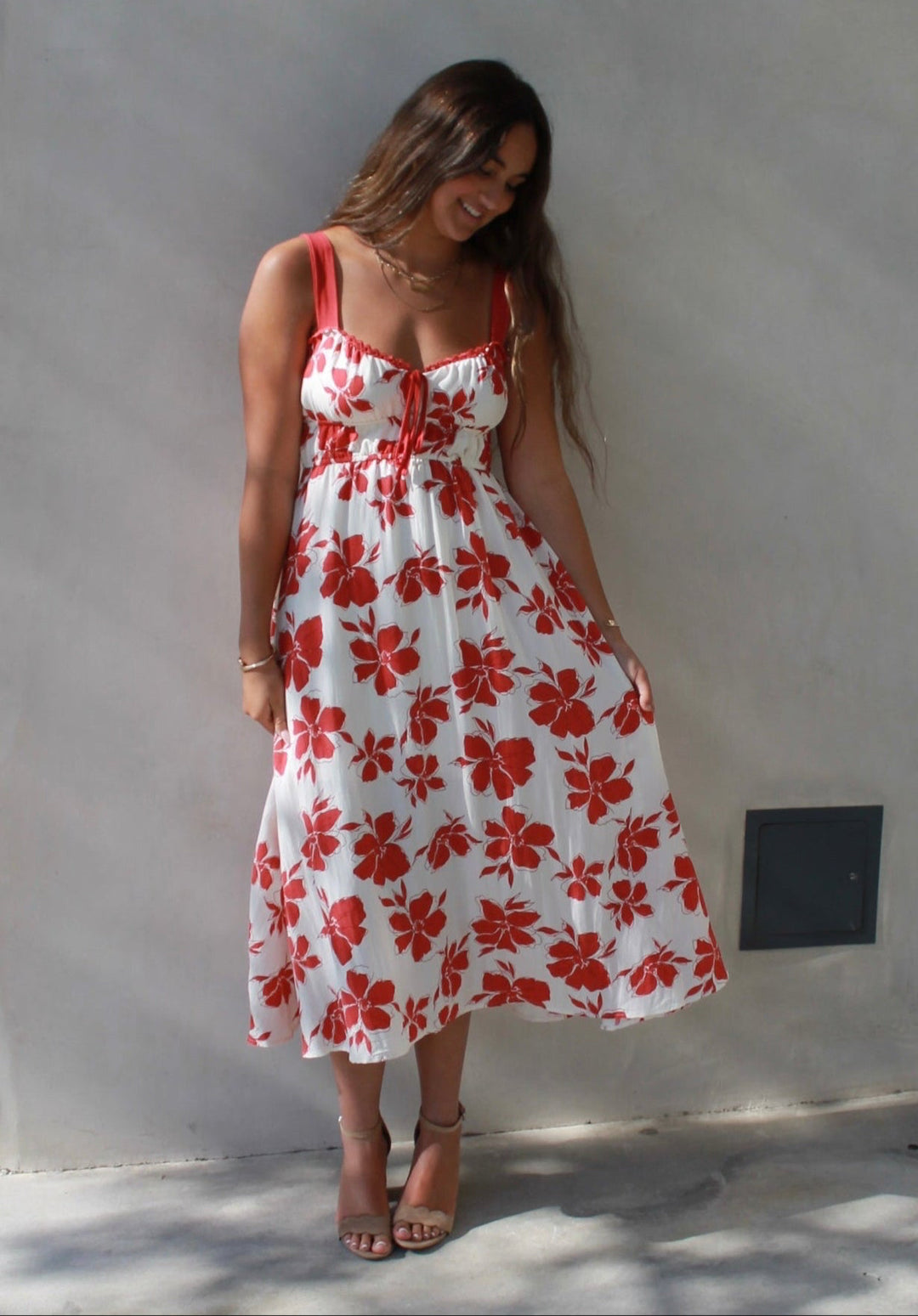 Woman in a red and white floral dress standing against a white wall on a city street.