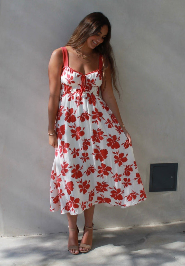 Woman in a red and white floral dress standing against a white wall on a city street.