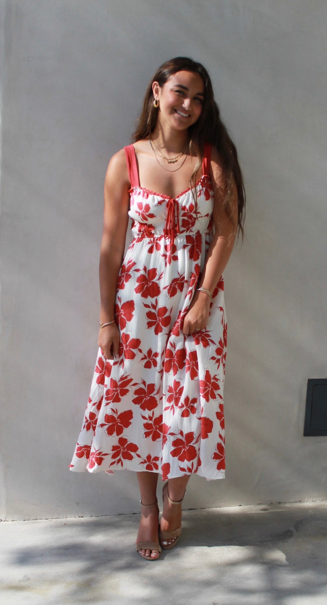 Woman in a red and white floral dress standing against a plain wall.
