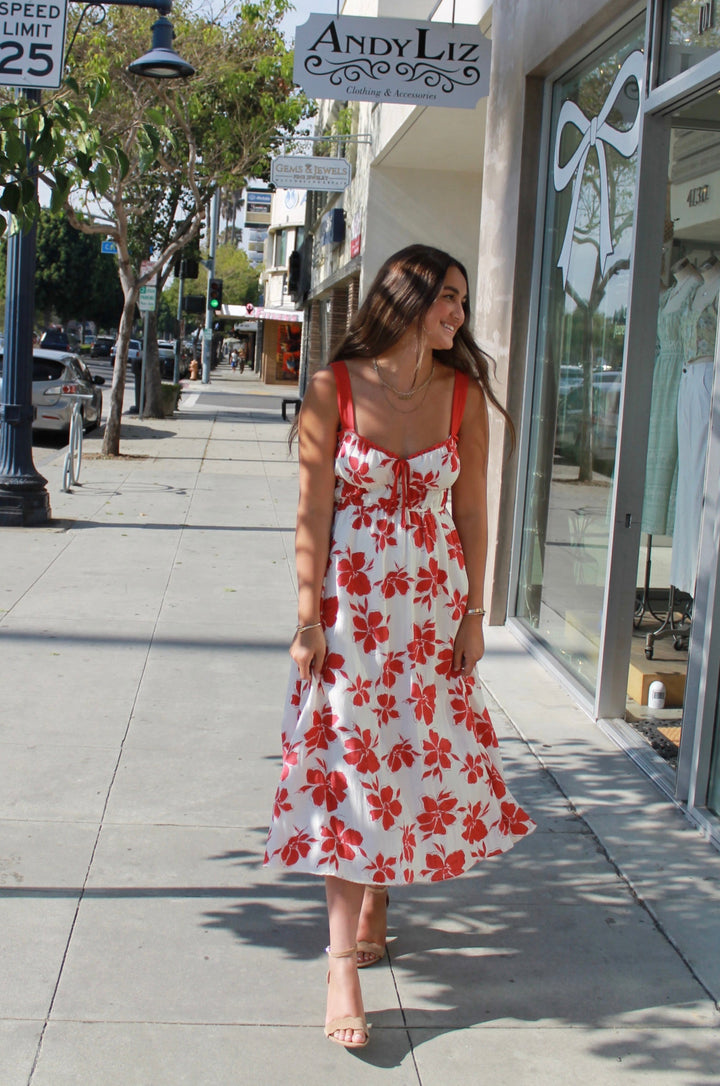 Woman in a floral dress walking on a sidewalk with a store and street signs in the background.
