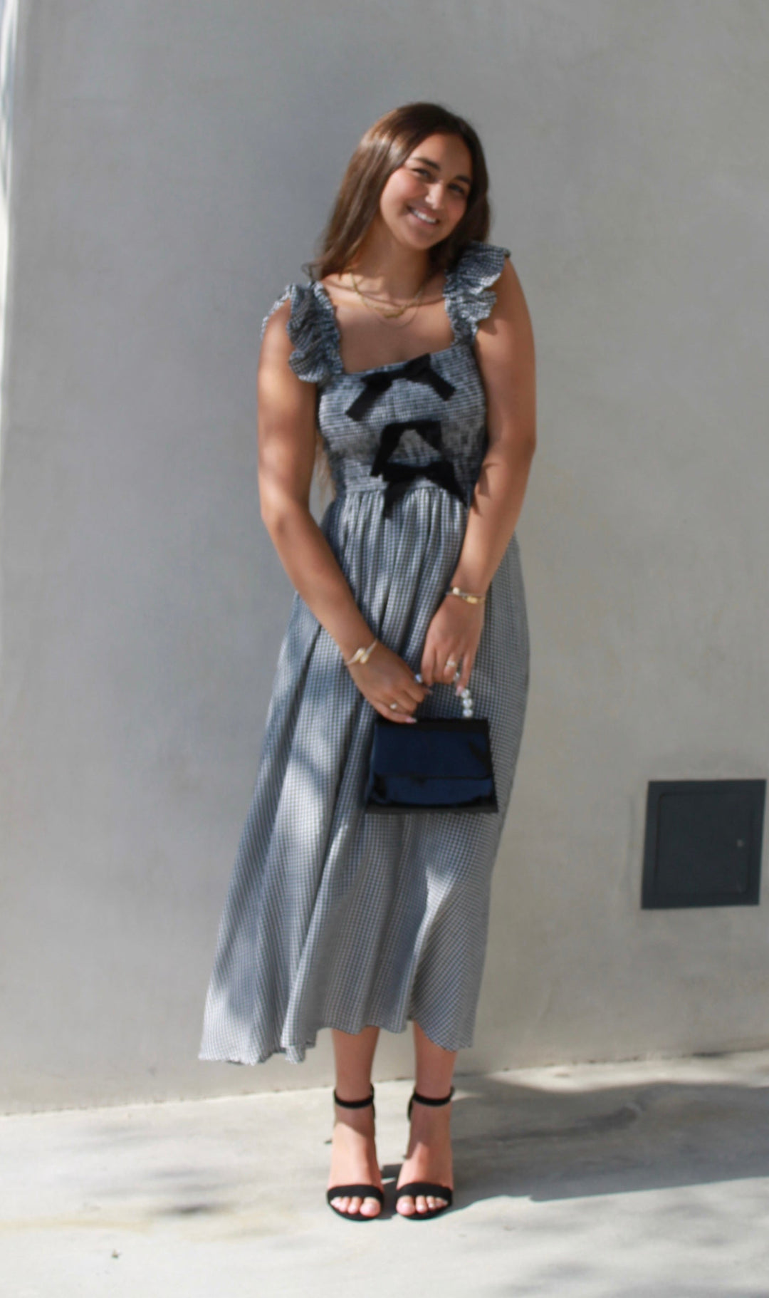 Woman in a gray dress standing against a plain wall.