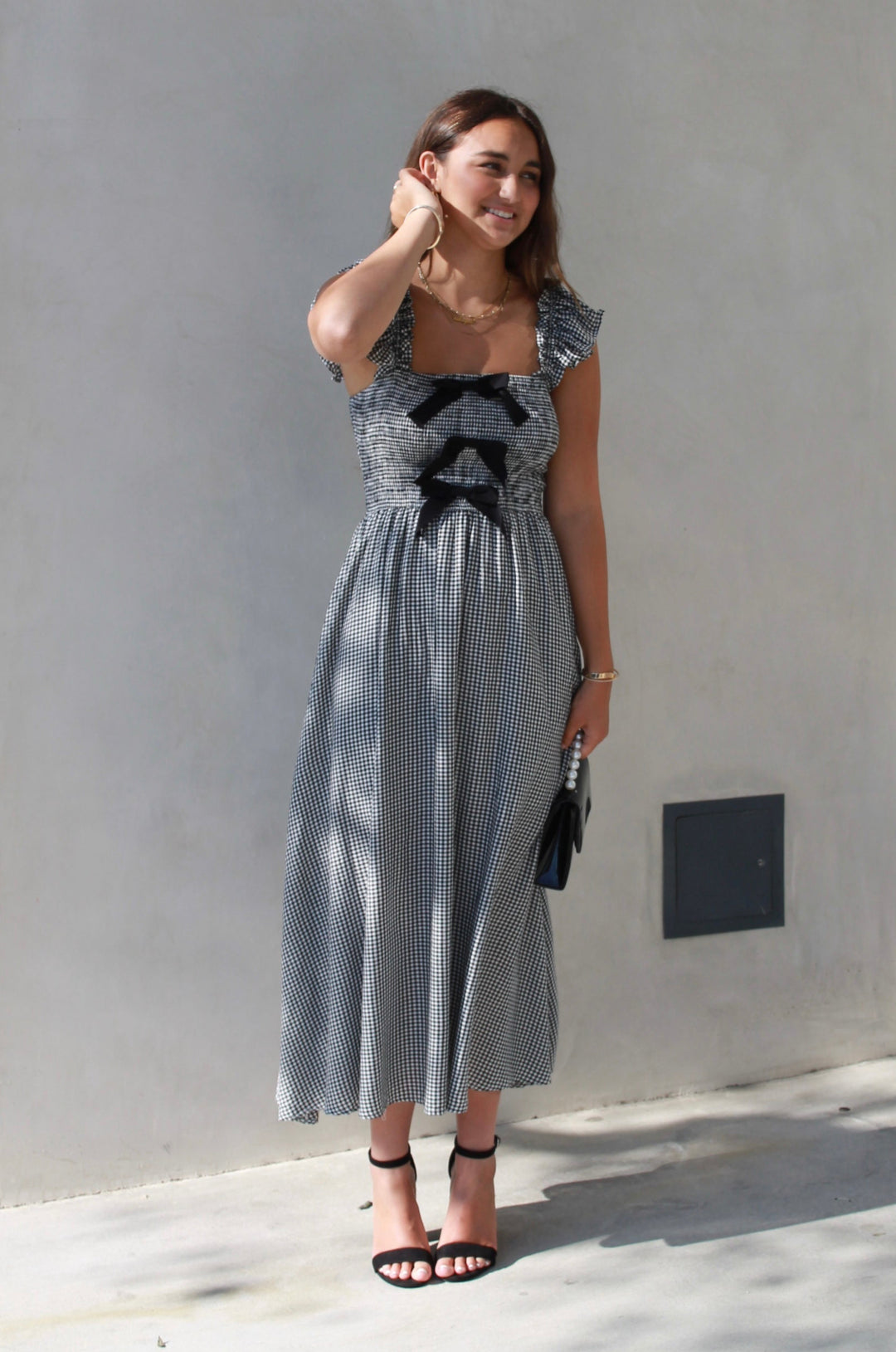 Woman wearing a gray dress with black floral patterns against a gray wall.