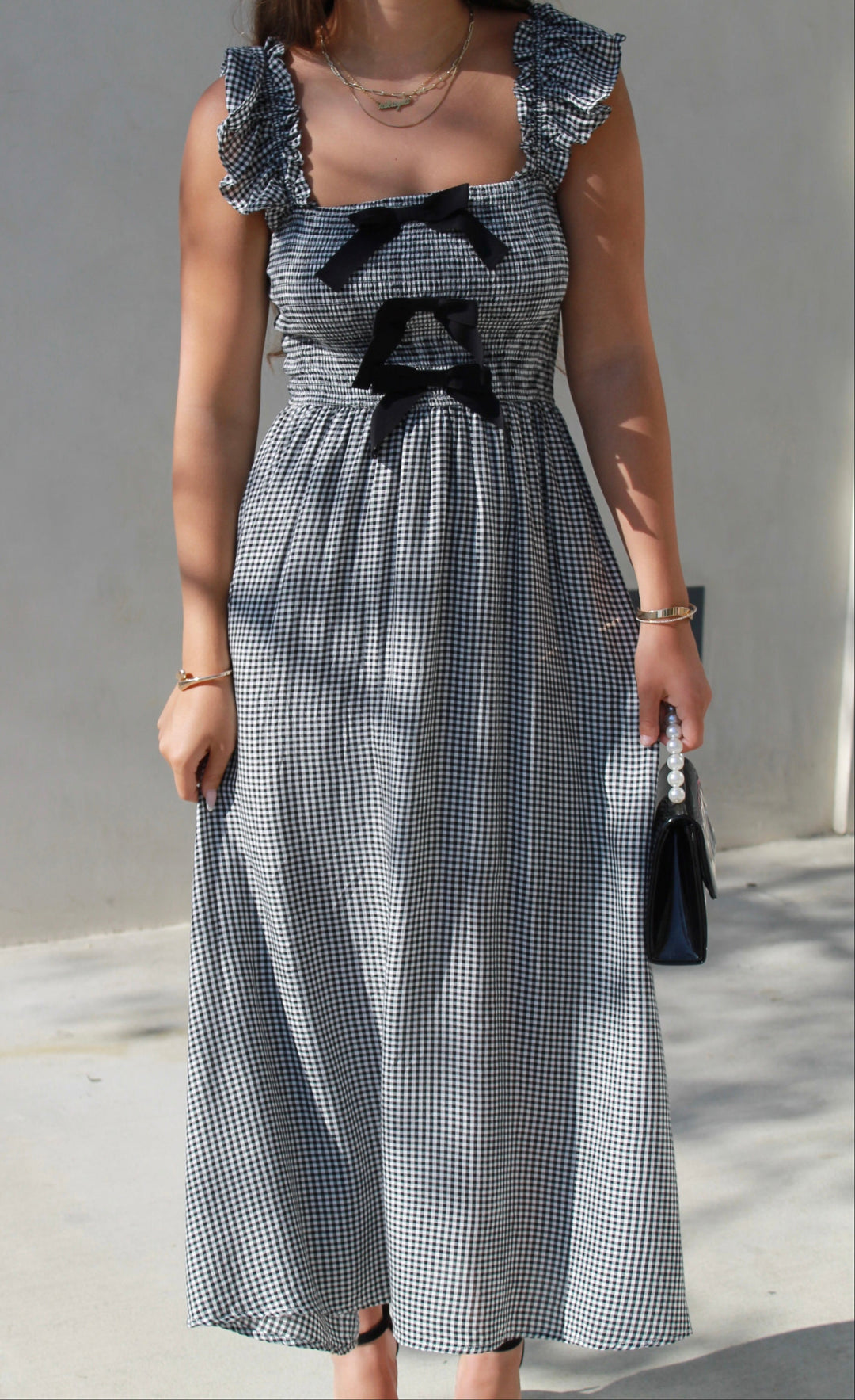 Woman wearing a checkered dress with ruffled straps and black bows outdoors.