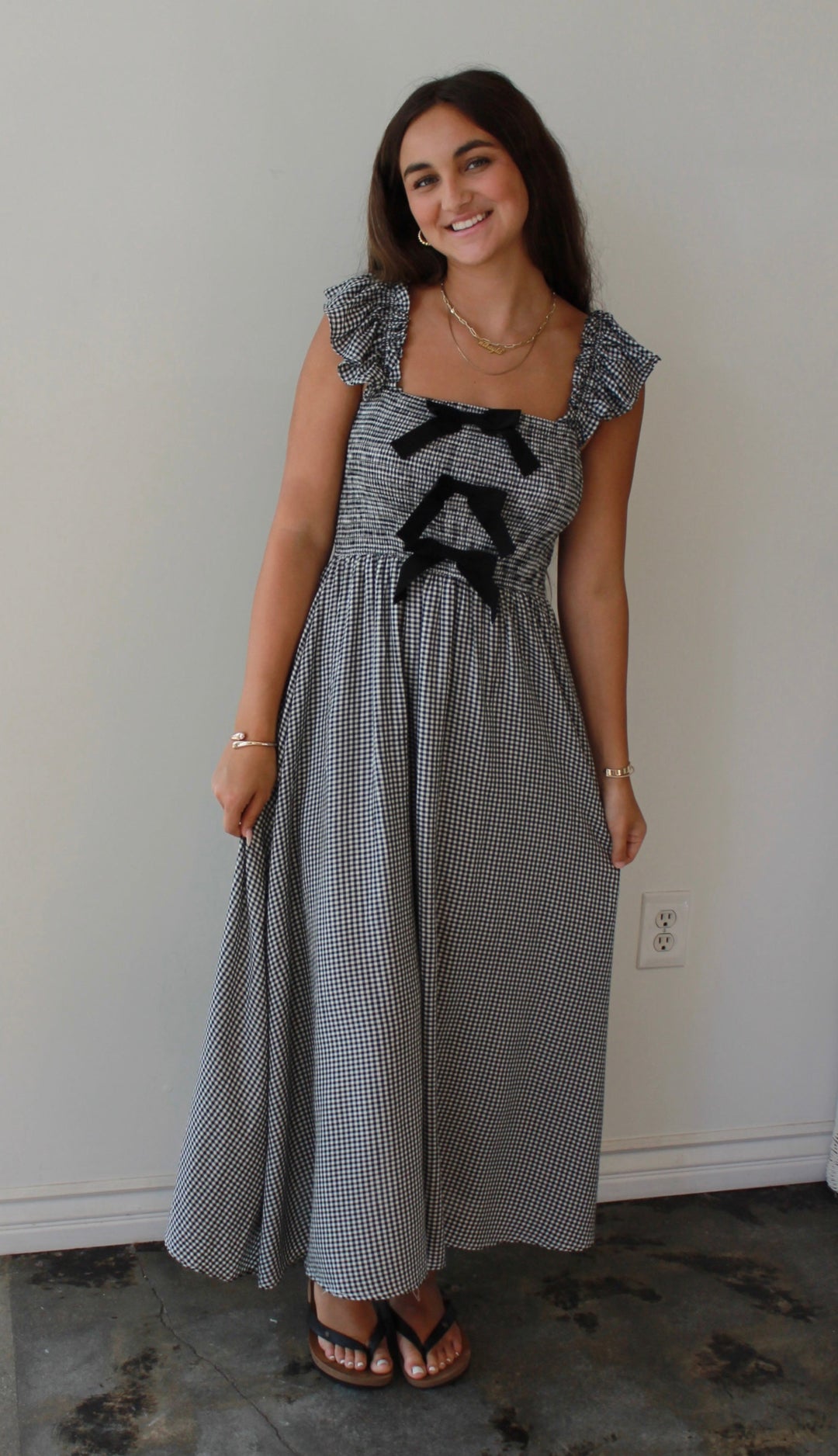 Woman wearing a gray dress with black bows standing in a room with a white wall and window.