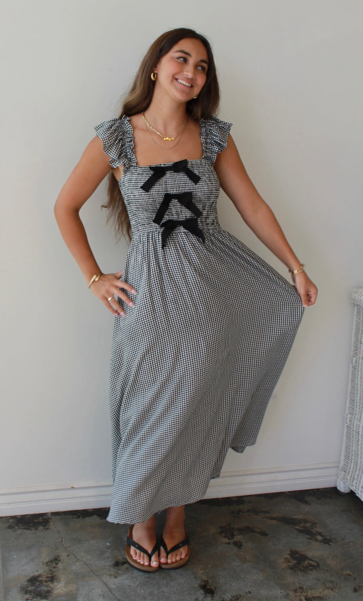 Woman wearing a gray dress with black bow details in a minimal indoor setting.