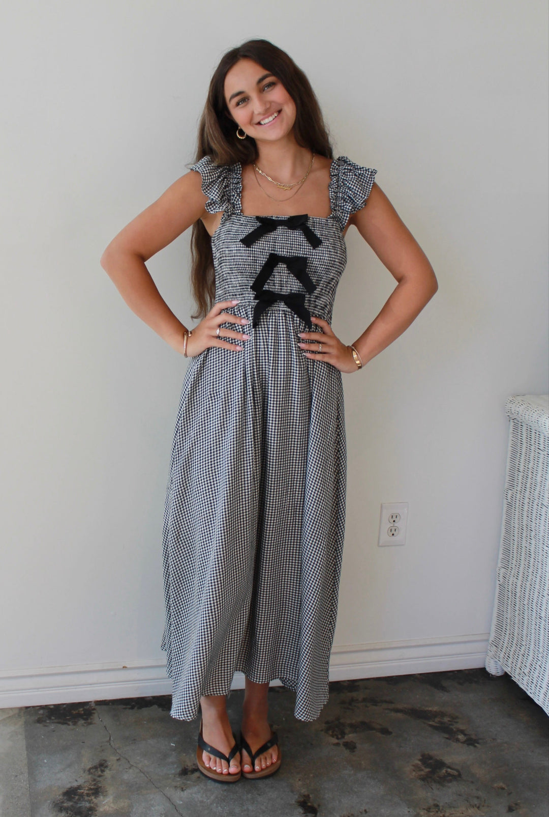 Woman wearing a gray checkered dress with black bow details in a minimal room.