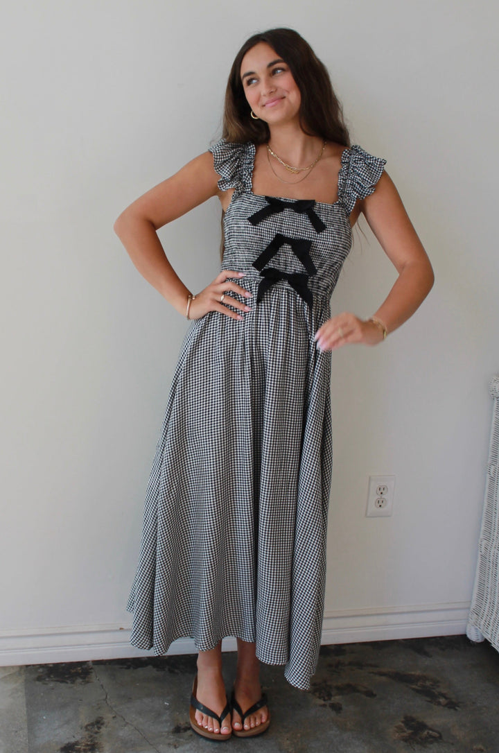 Woman wearing a patterned dress standing in a room with a white wall and window.