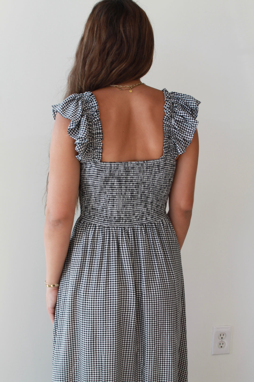 Woman wearing a black and white checkered dress with ruffled shoulders against a plain background