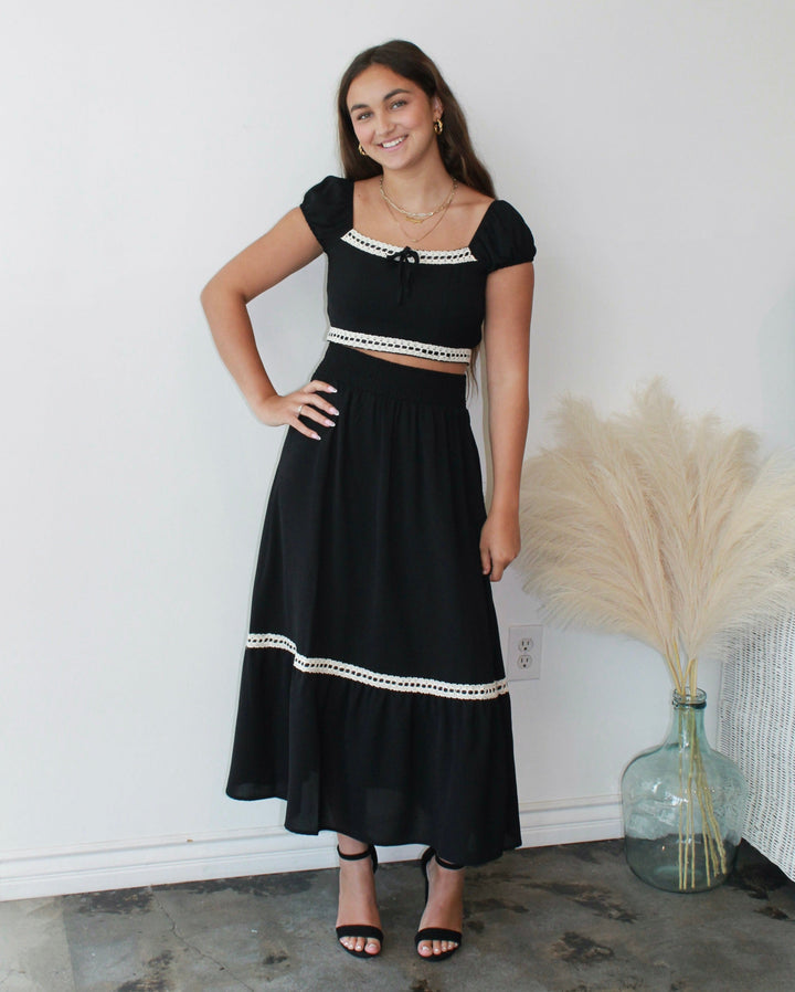 Woman wearing a black dress with white trim standing against a white wall.