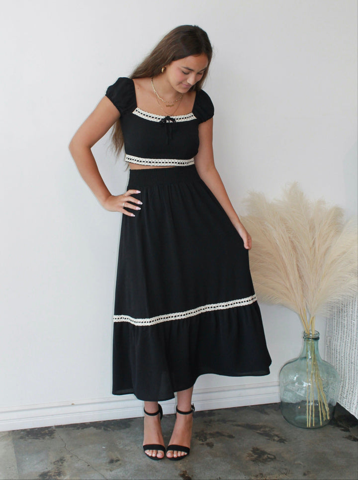 Woman wearing a black dress with white trim against a white wall.