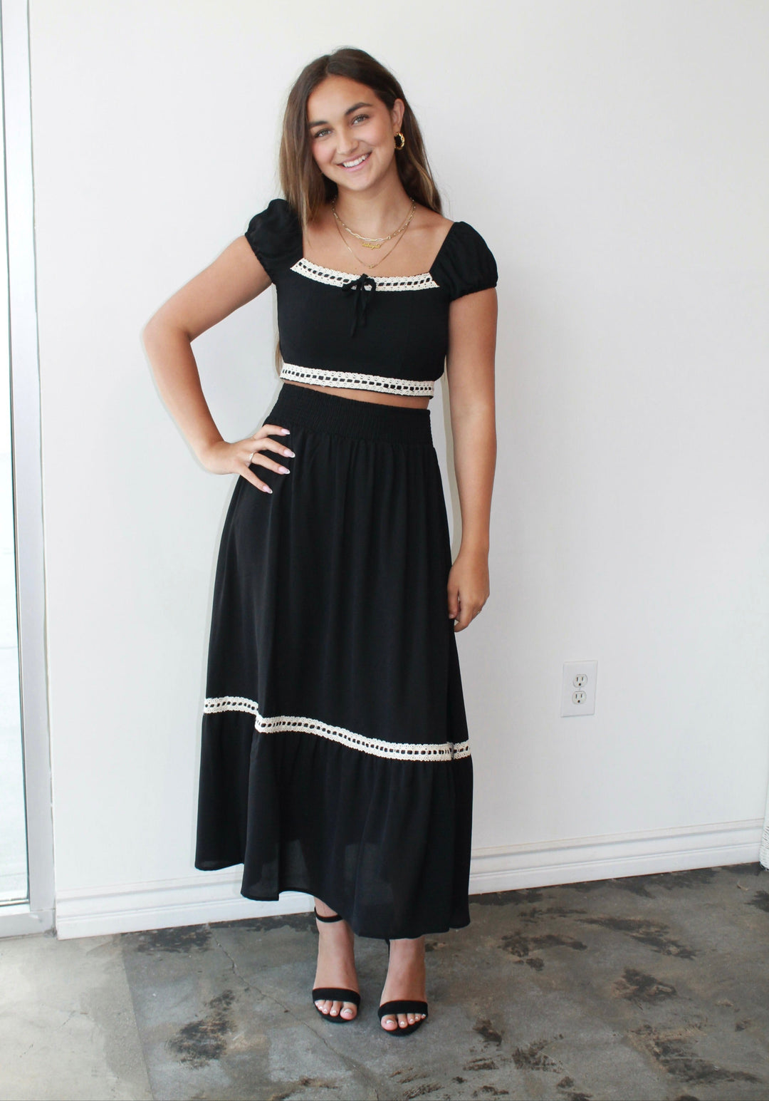 Woman wearing a black outfit with white trim standing against a white wall.