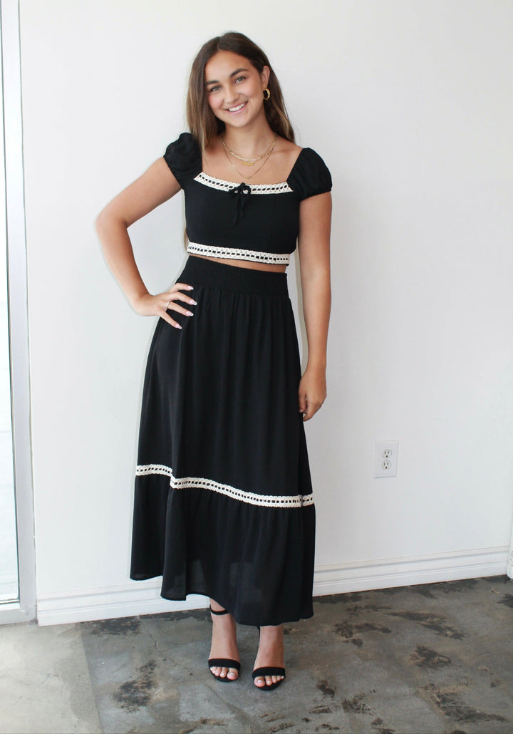 Woman wearing a black outfit with white trim standing against a white wall.