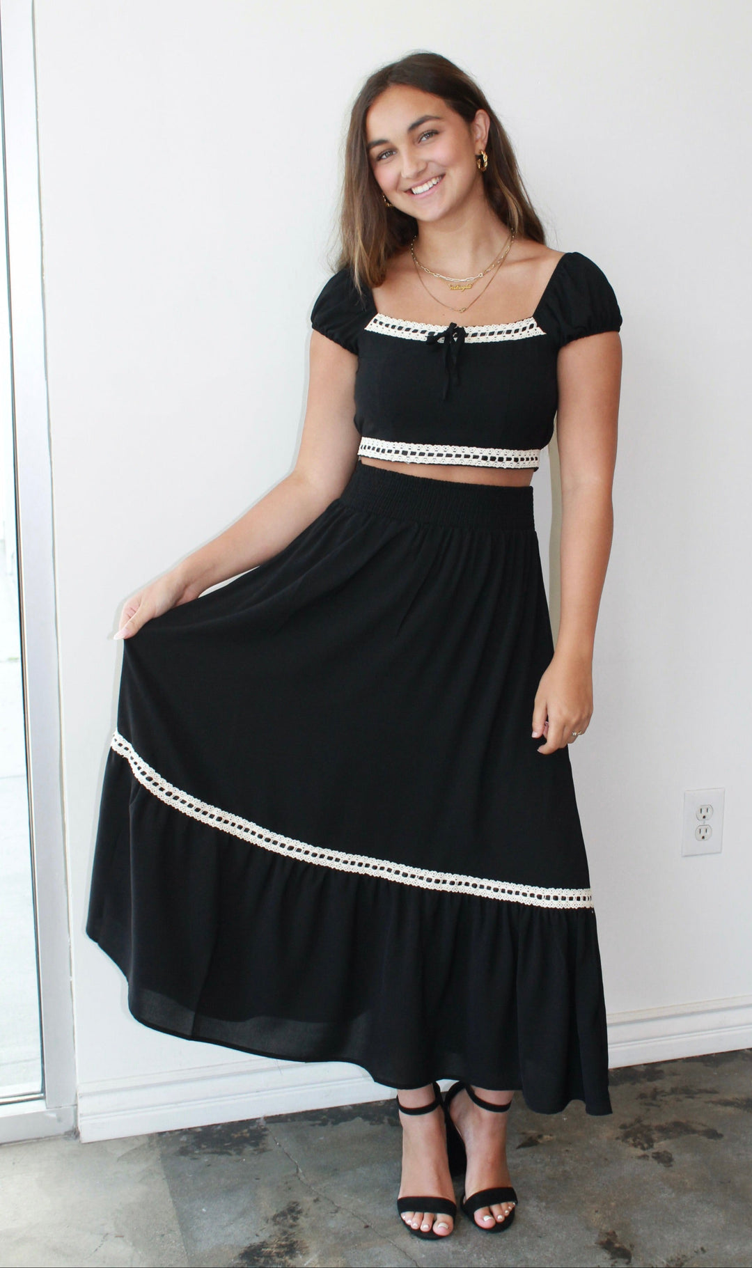 Woman wearing a black skirt set with white trim against a white wall.