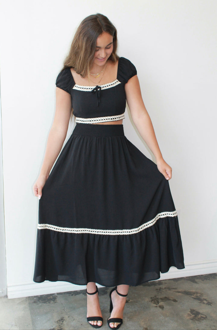 Woman wearing a black skirt set with white trim against a white wall.