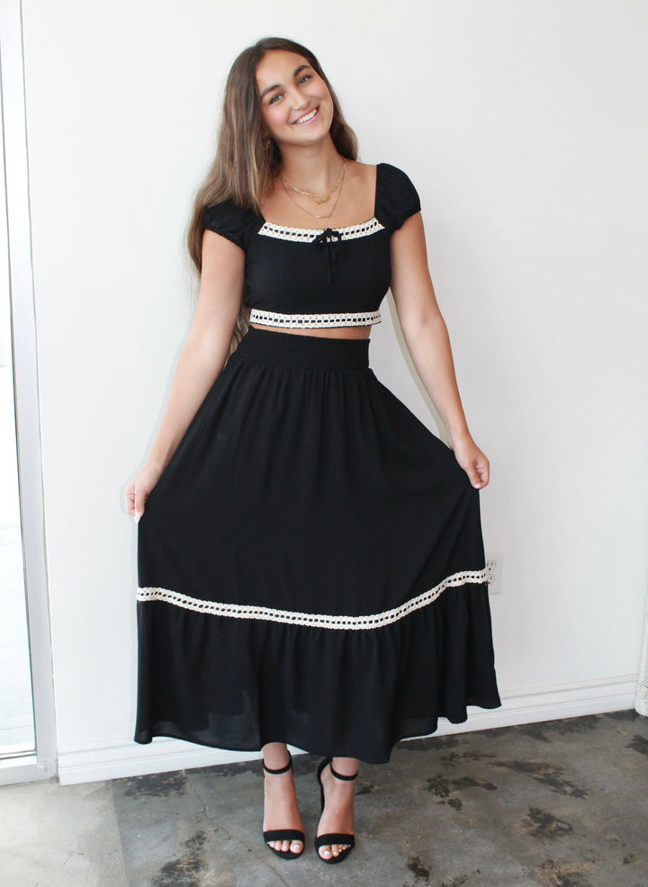 Woman wearing a black dress with white trim against a white wall.