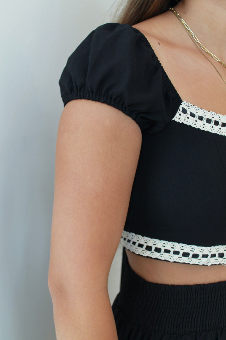 Black top with white lace trim worn by a person against a plain background