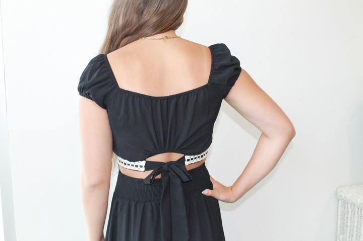 Woman wearing a black top with cut-out design and skirt against a white background