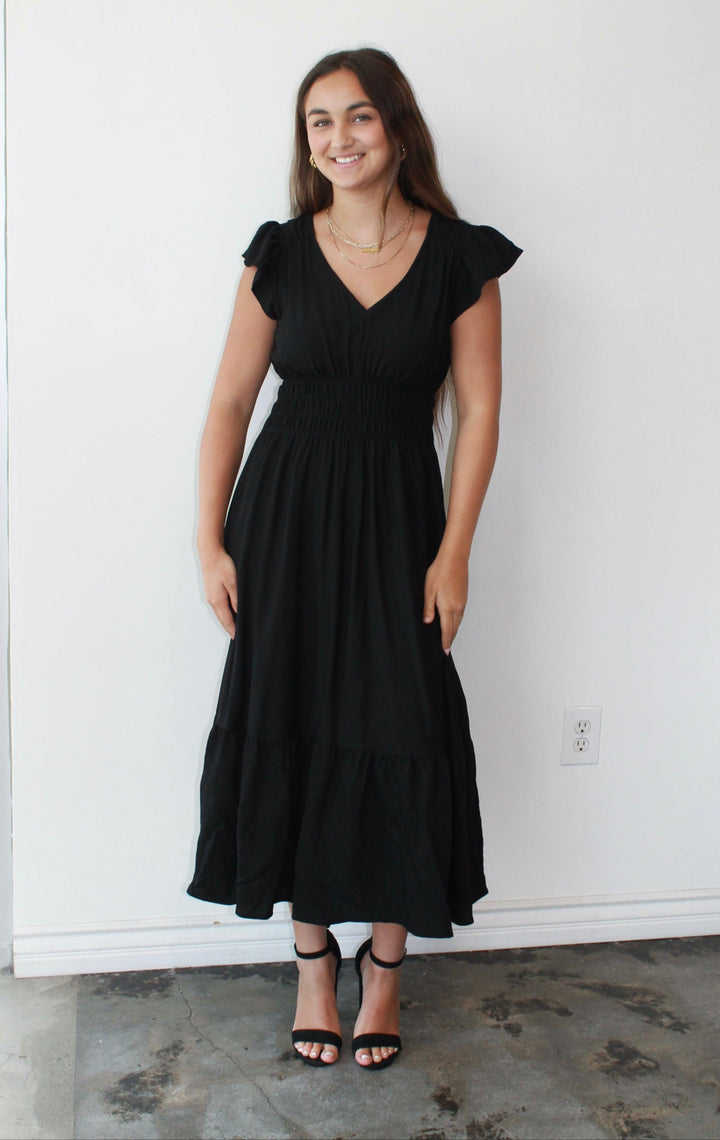 Woman wearing a black dress standing against a white wall.