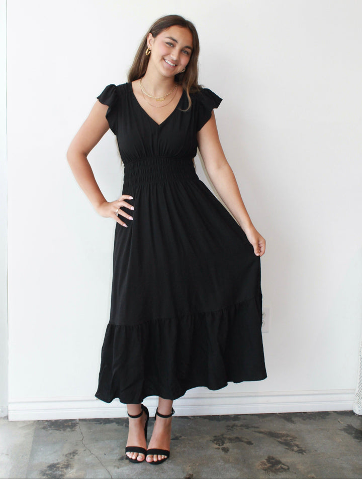 Woman wearing a black dress standing against a white wall.