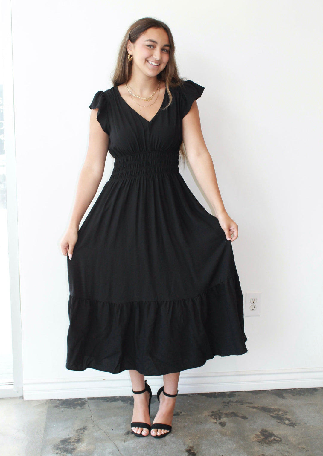Woman wearing a black dress standing against a white wall.