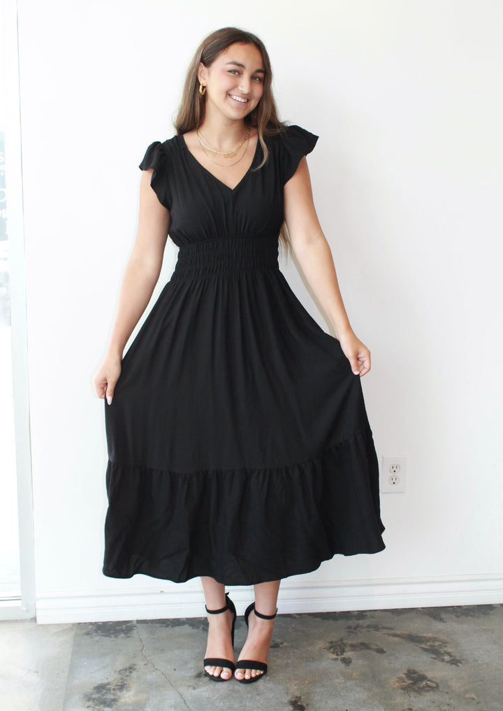 Woman wearing a black dress standing against a white wall.