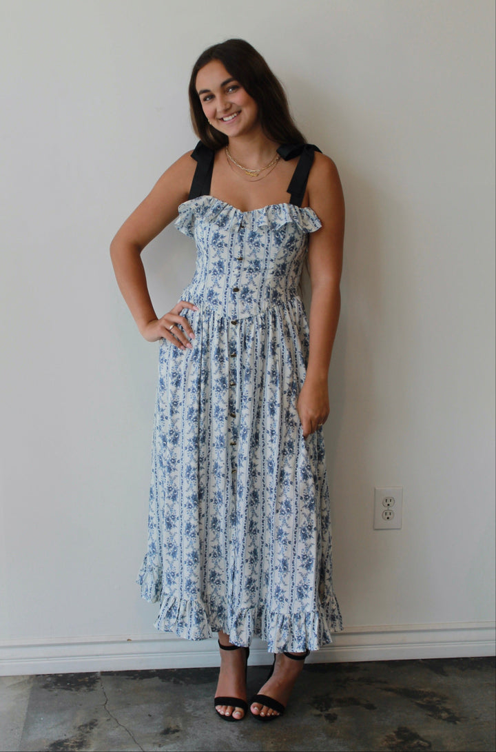 Woman wearing a floral dress standing against a white wall.