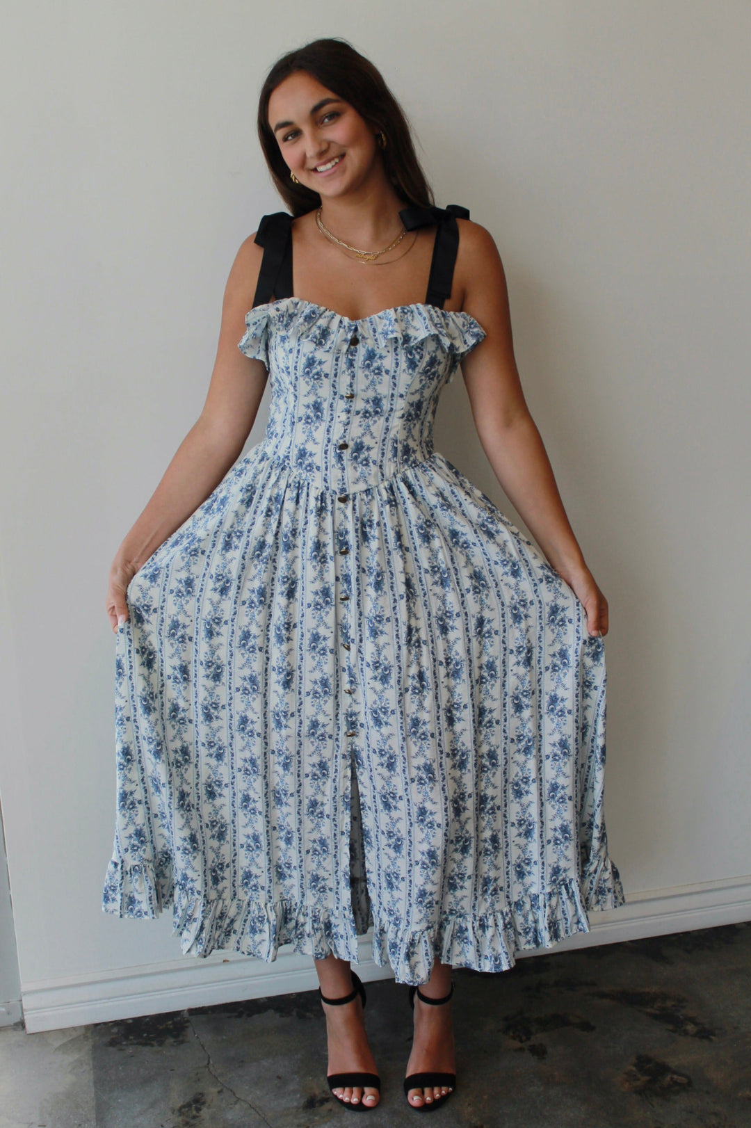 Woman wearing a floral dress standing against a plain wall.