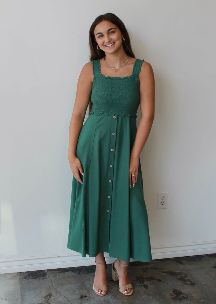 Woman wearing a green dress standing against a white wall.