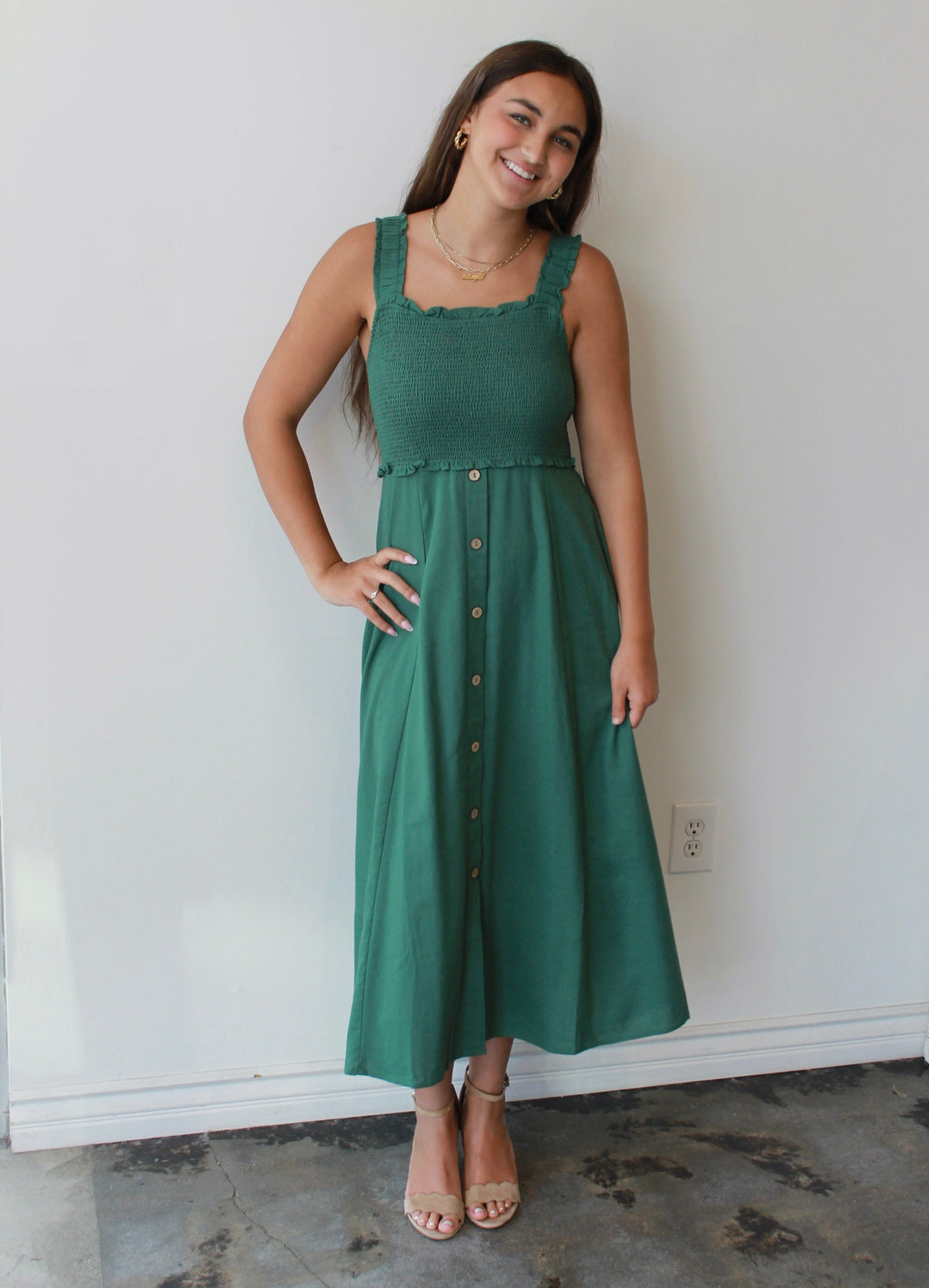 Woman wearing a green dress standing against a white wall.