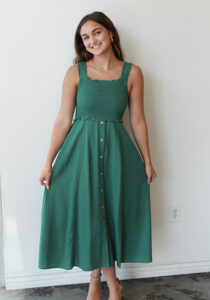 Woman wearing a green dress standing against a white wall.
