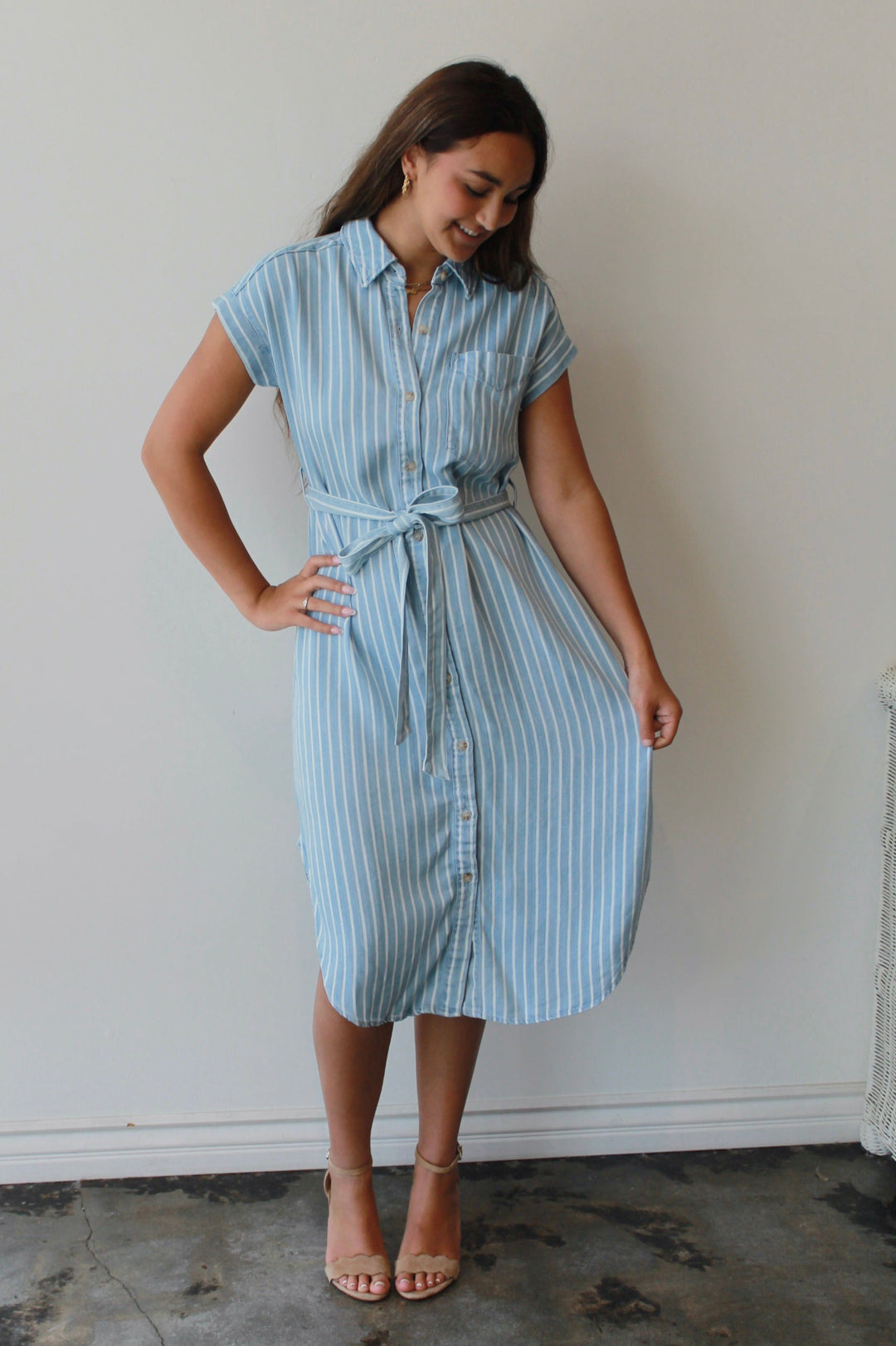 Woman wearing a light blue striped dress against a white wall.