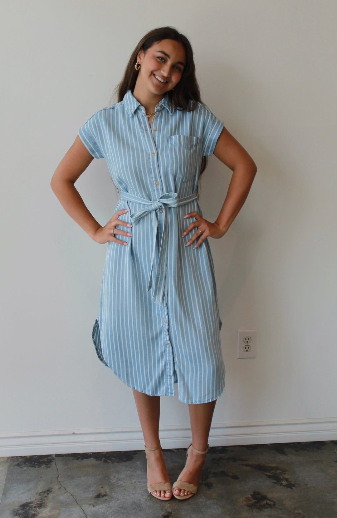 Woman wearing a blue striped dress standing against a white wall.