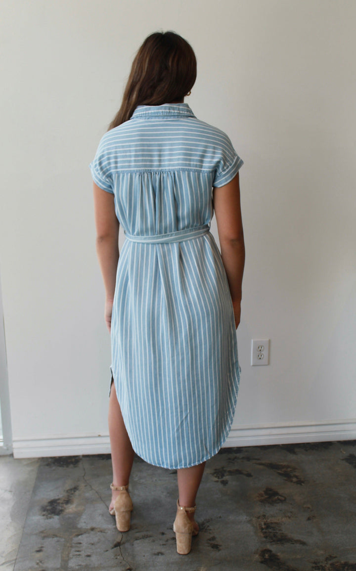 Woman wearing a light blue striped dress standing in a room with a white wall and floor.