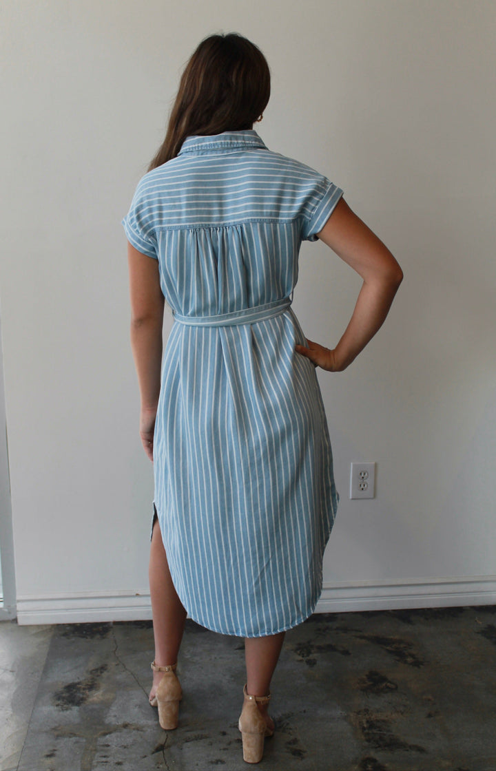 Woman wearing a blue striped dress standing in a room with a white wall.