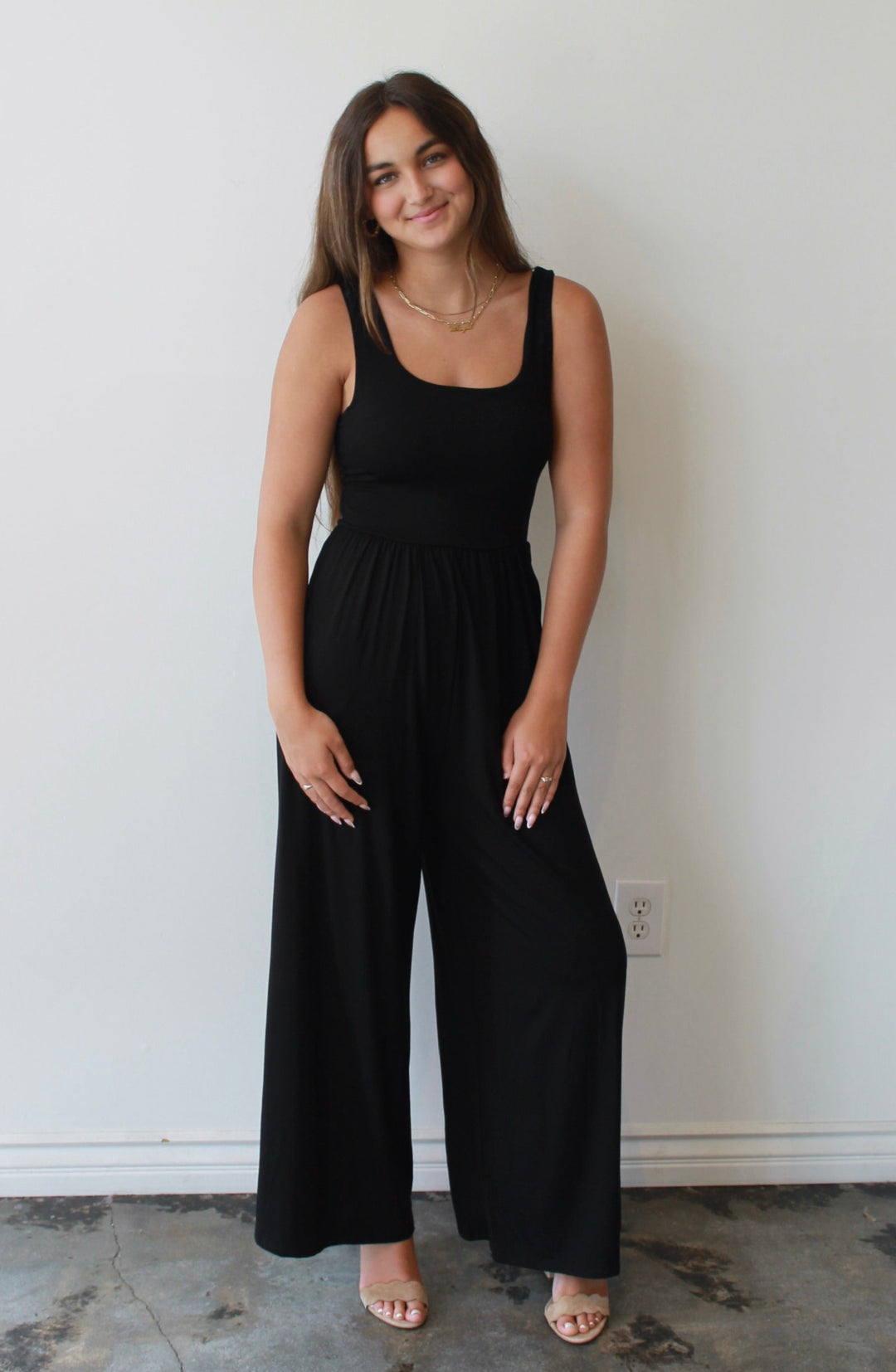 Woman wearing a black jumpsuit standing against a white wall.
