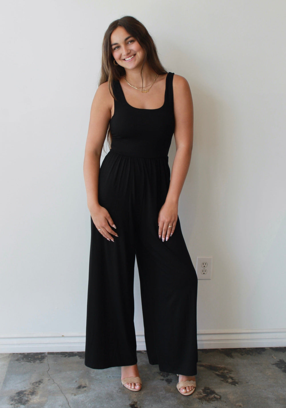 Woman wearing a black jumpsuit standing against a white wall.