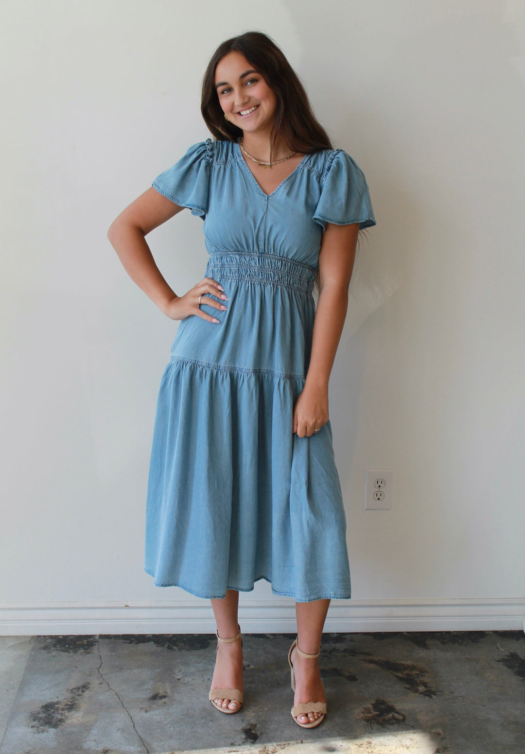 Woman wearing a blue dress standing against a white wall.