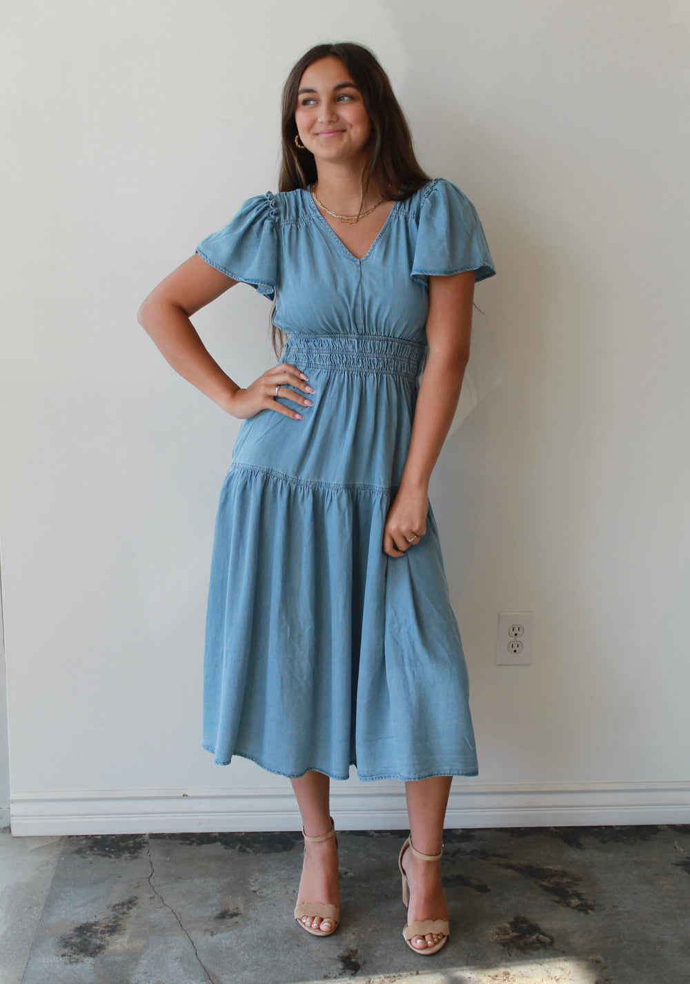 Woman wearing a blue dress standing against a white wall.