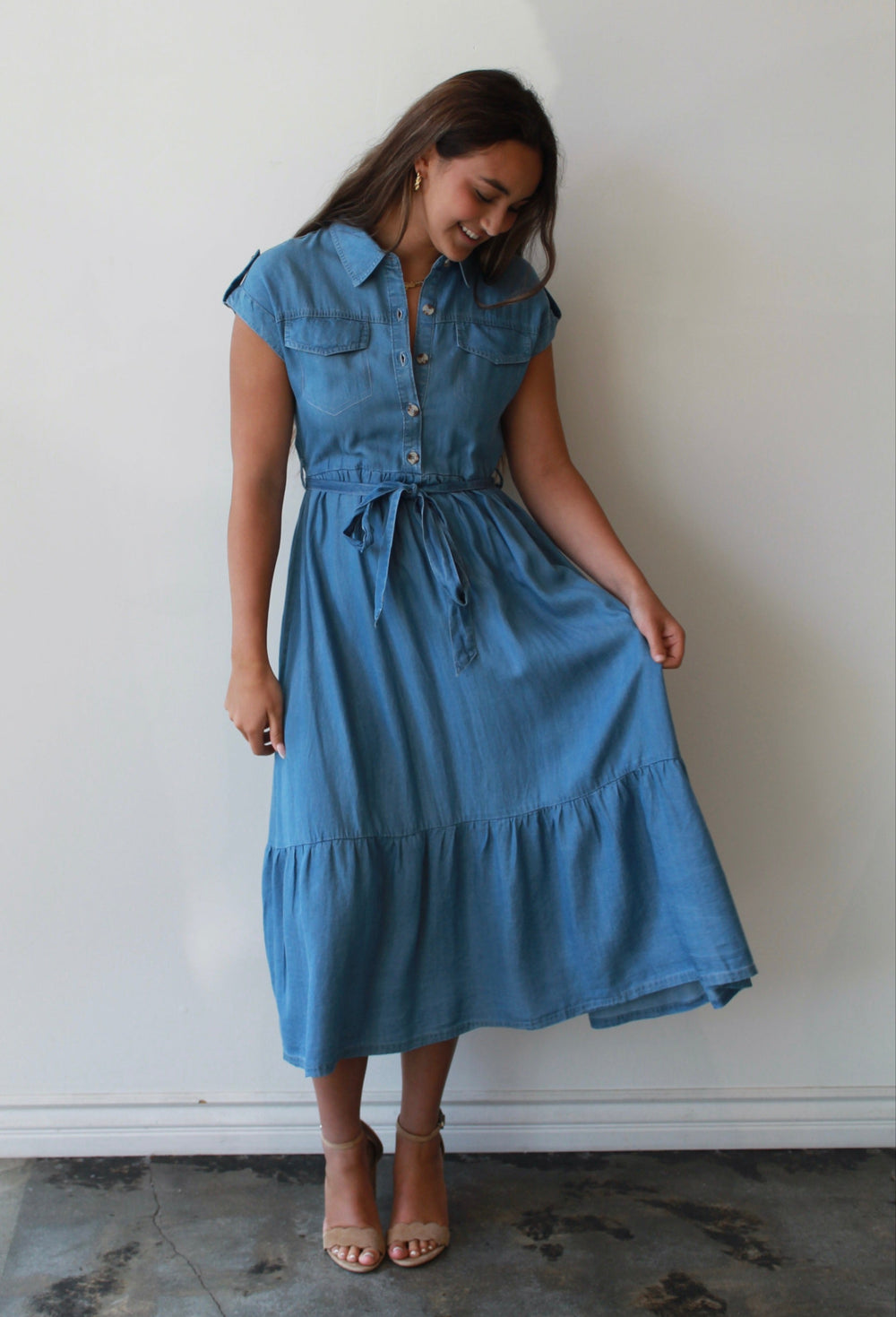 Woman wearing a blue dress standing against a white wall.