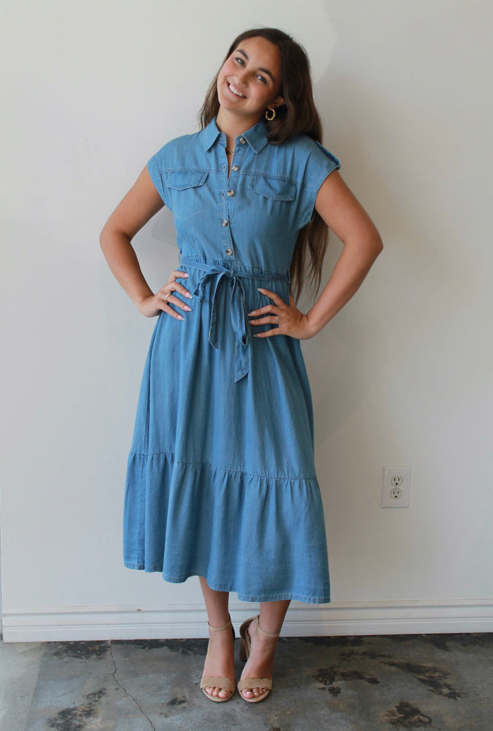 Woman wearing a blue dress standing against a white wall.