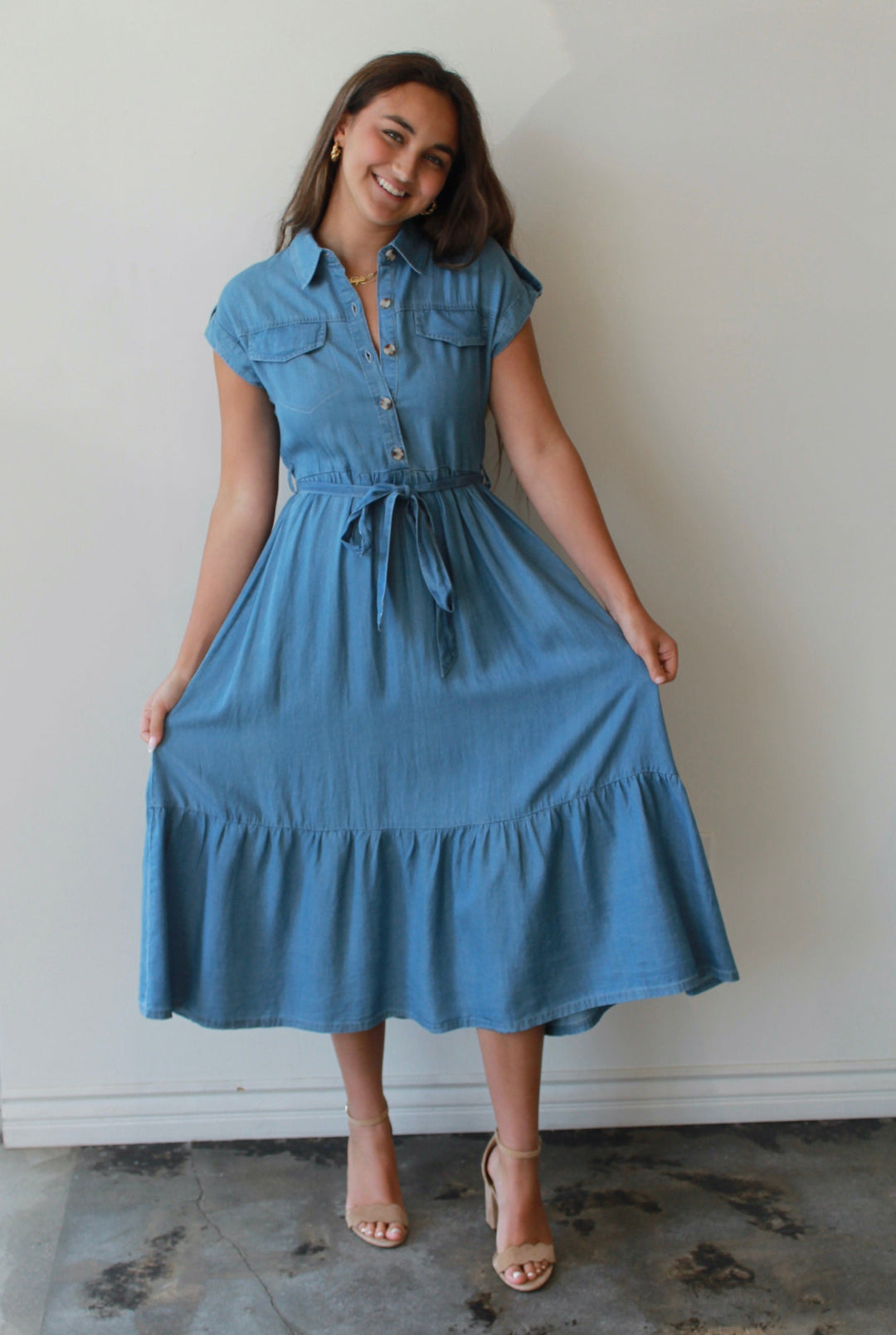 Woman wearing a blue dress standing against a white wall.